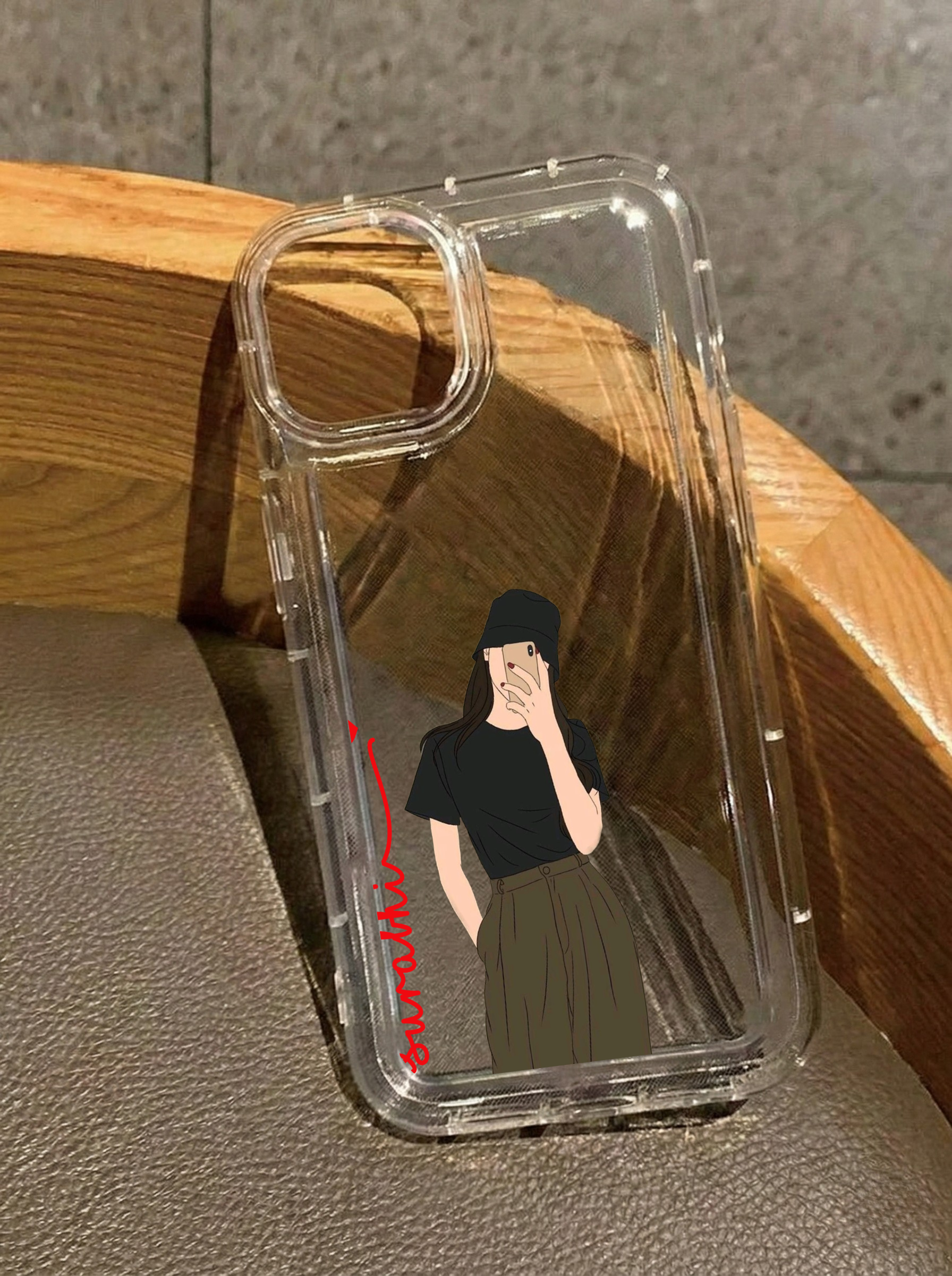 Clear iPhone 16 case featuring an illustrated girl wearing a black t-shirt, green cargo pants, and a bucket hat, with the customized name Surabhi in vertical red text.